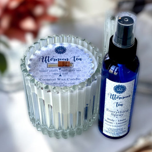 Coconut wax candle and 'Afternoon Tea' spray bottle on a white surface with flowers in the background